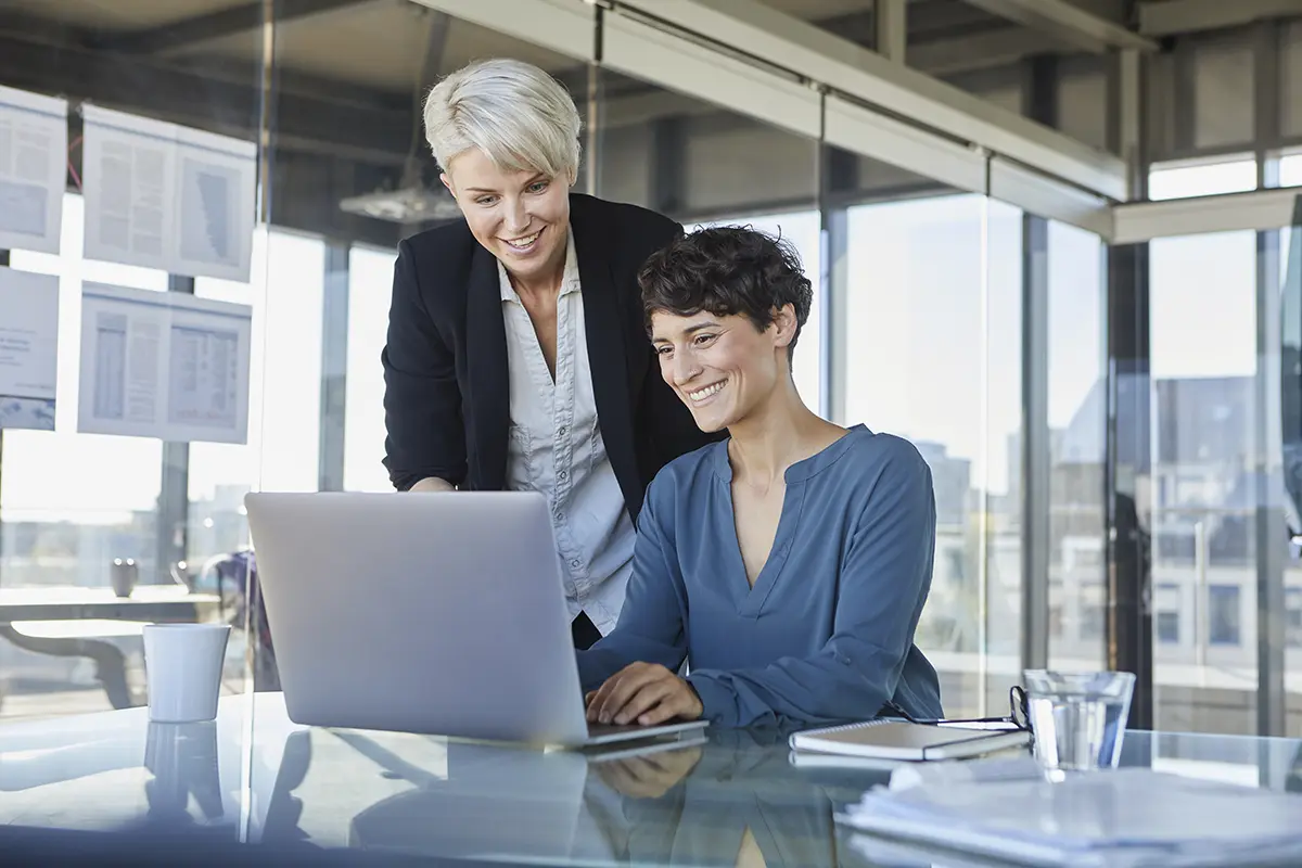 two smiling businesswomen sharing laptop at desk i 2024 09 13 20 33 26 utc 1 1.webp